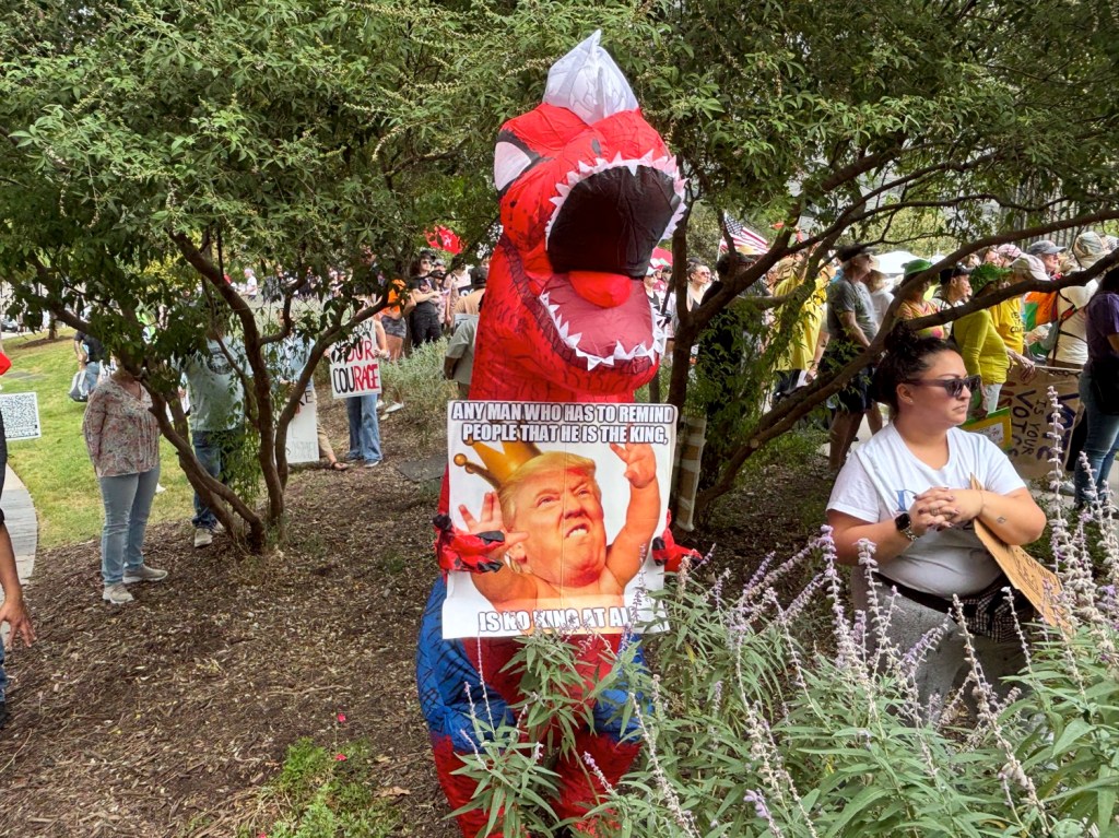 Man in dinosaur costume holding anti-Trump sign in Dallas.